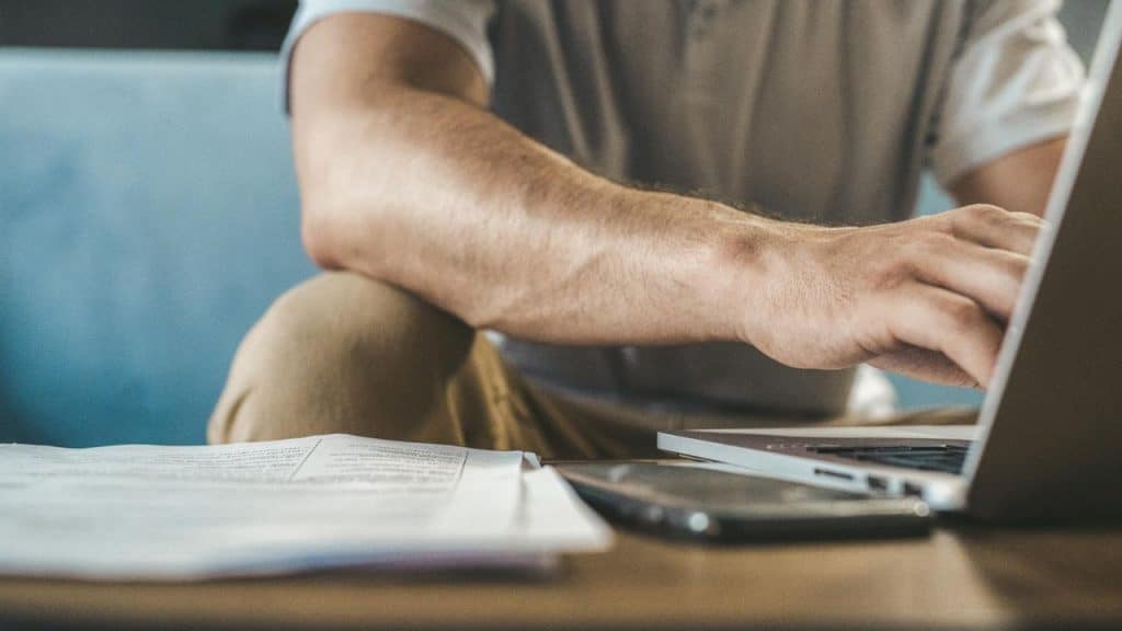 Close-up of a person's hands typing on a laptop next to a smartphone and papers.
