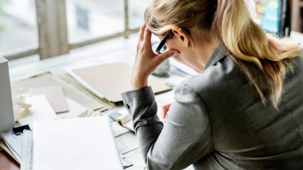 A person holding their head in distress as they read documents on a table.