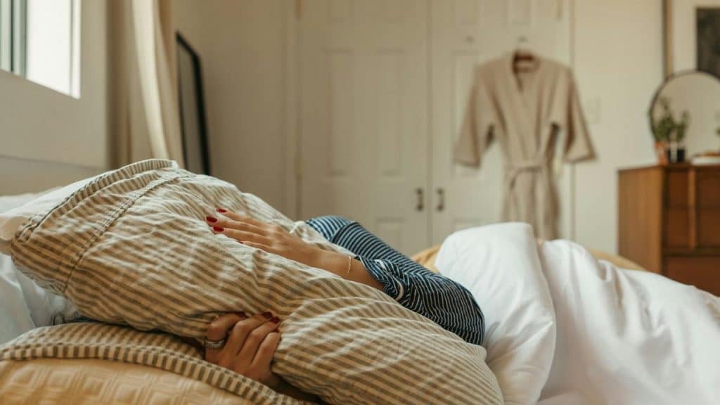 A person lying in bed hugging a pillow in a calm bedroom.