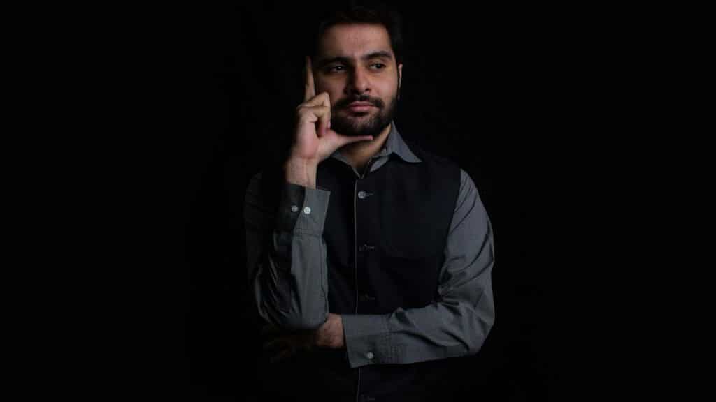 A thoughtful bearded man in a dark vest posing against a black background.