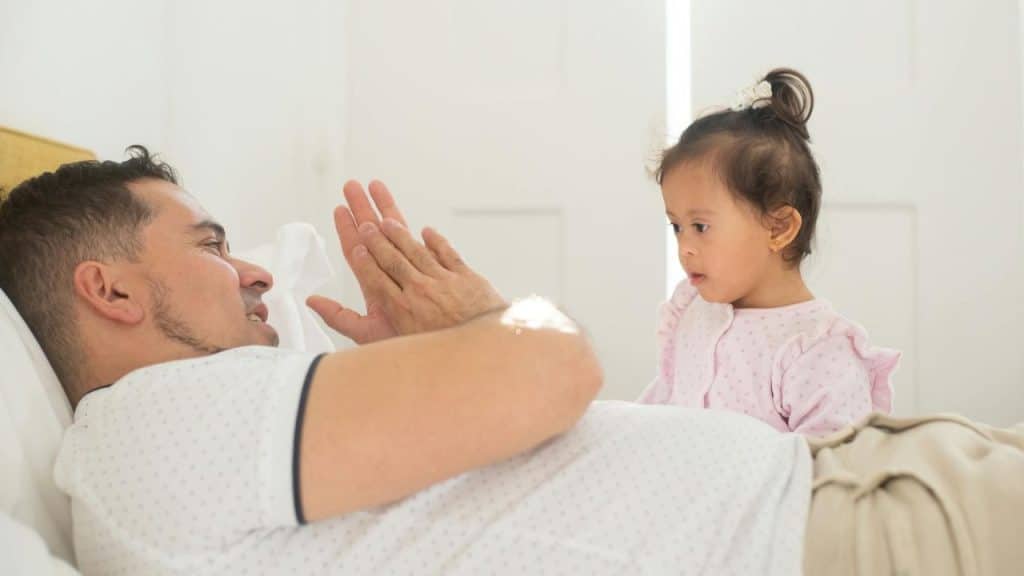 A man lying down claps his hands together while looking at a young girl in pink.