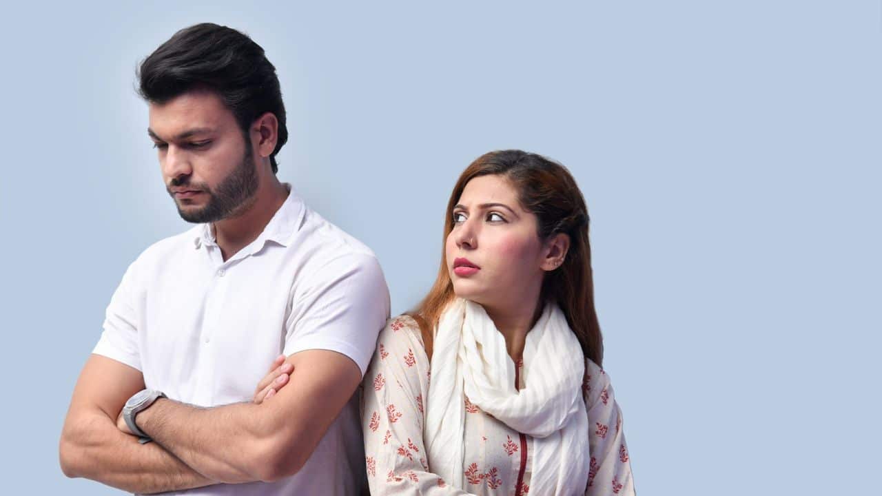 A man with crossed arms stands back-to-back with a woman who looks at him.