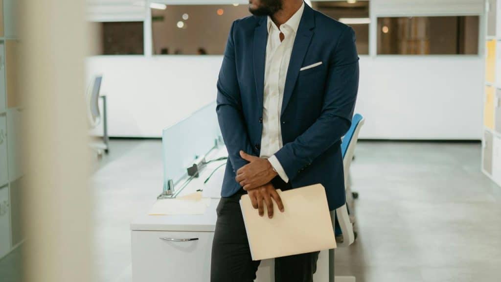 A person in a blue blazer standing in an office holding a folder.
