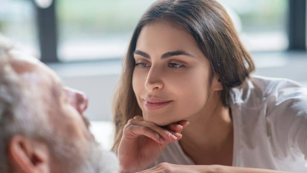 A woman staring at an older man while lying on his chest and holding her chin on the back of her hand.