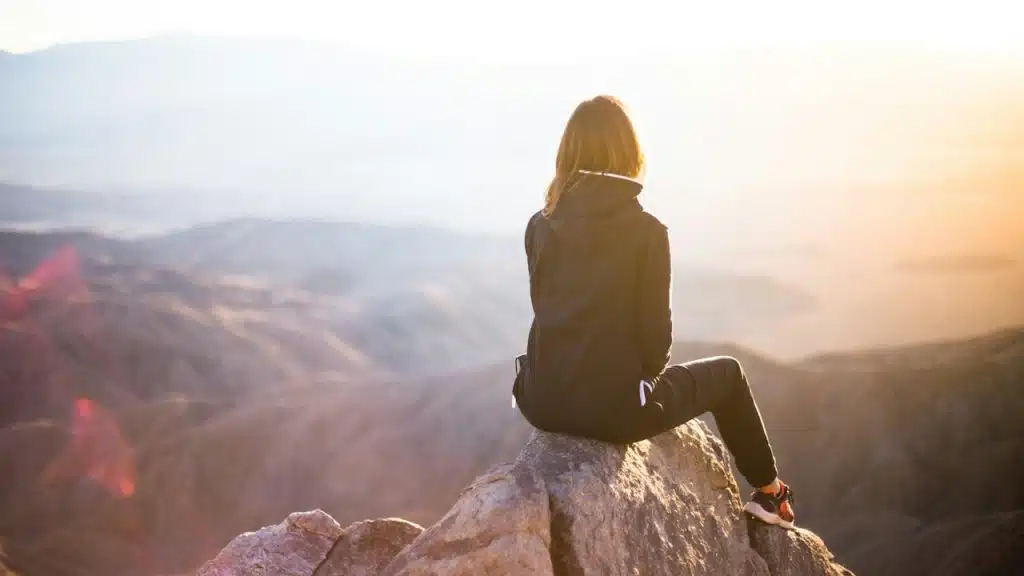 A woman dressed in black is sitting on a peak of a hill.