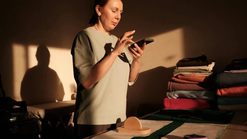 A person standing indoors and using a smartphone near a table.