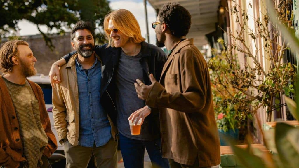 Four men stand together outdoors; one has his arm around another while they all talk.