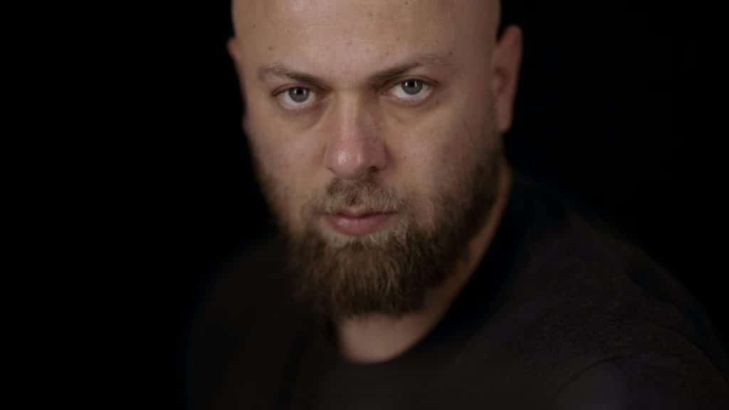 A close-up portrait of a bald man with a beard looking directly into the camera.
