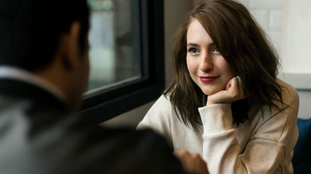 A woman with brown hair rests her chin on her hand while looking at a man.