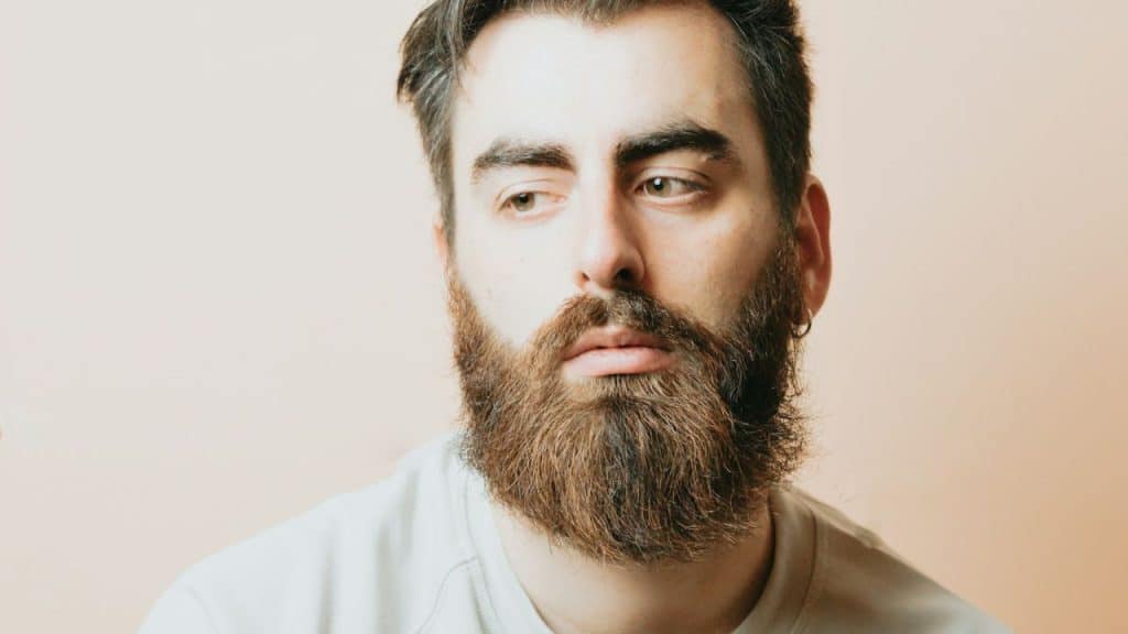 A man with a full beard and short hair looks pensively toward the side.