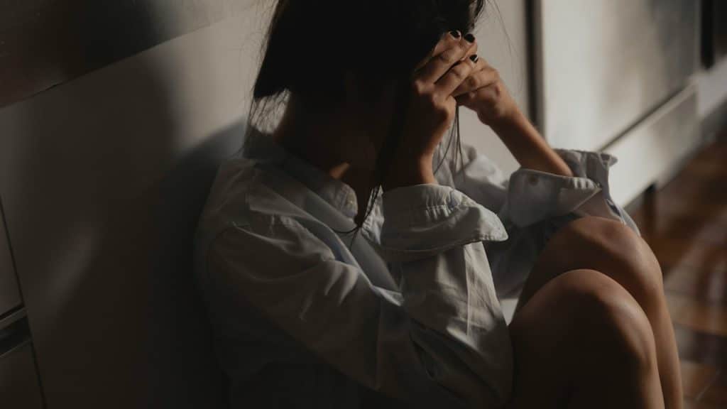 A woman sitting on the floor in a dimly lit room with her head in their hands.