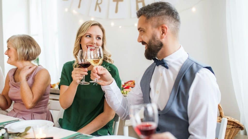 A smiling man and woman in formal attire toast with glasses of wine at a dinner.