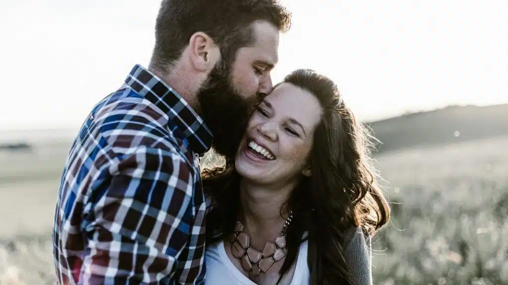 A man kissing his wife in an open field.