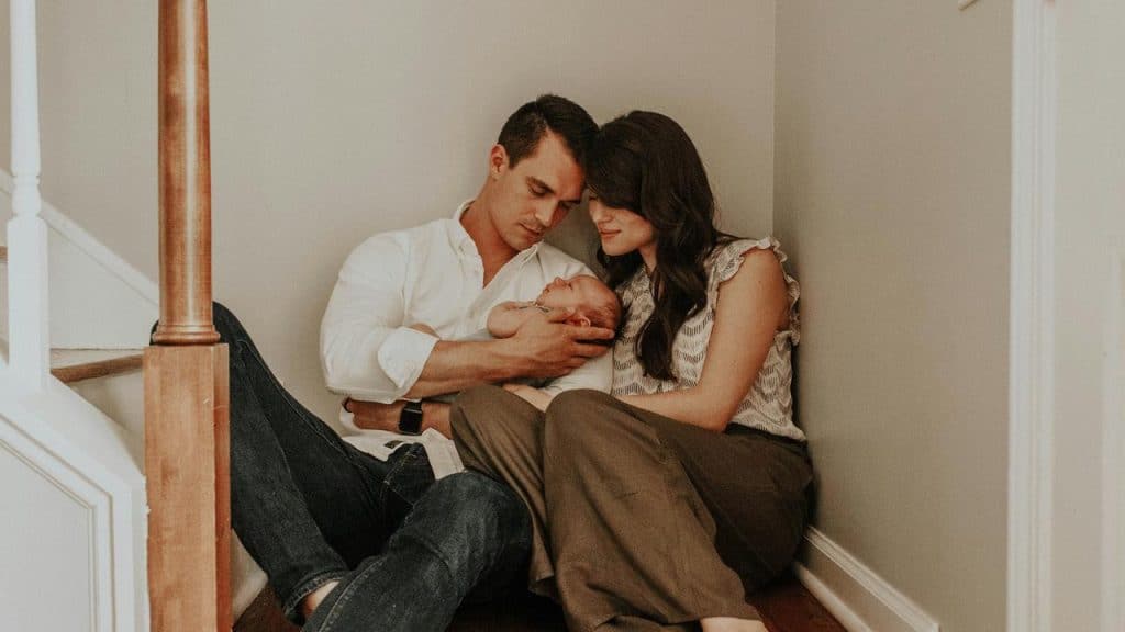 A couple sitting on stairs while tenderly holding a sleeping baby.