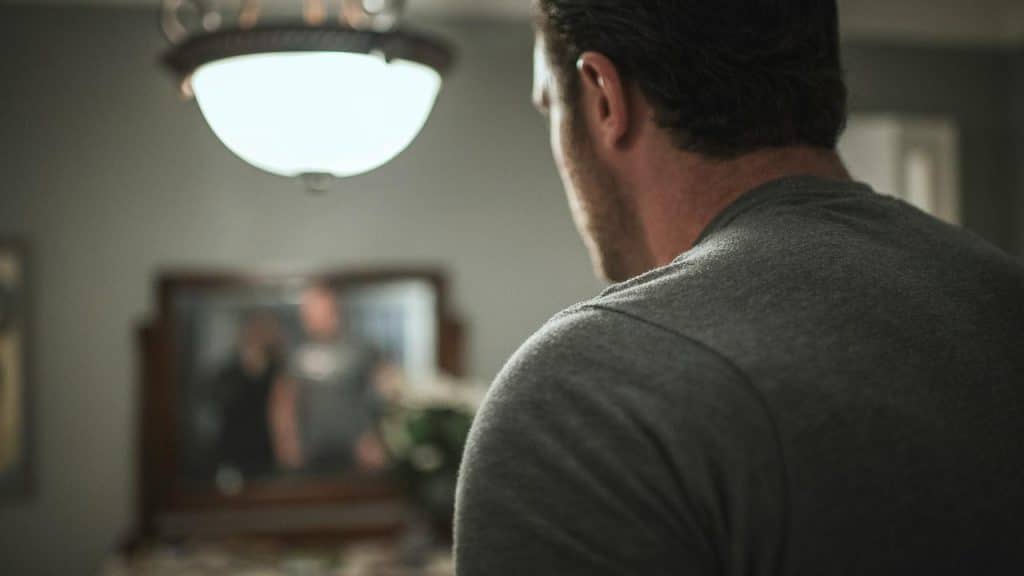 A man seen from behind looking at his reflection in a mirror.