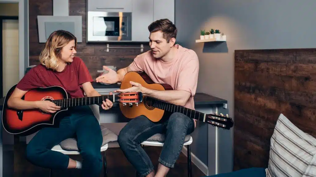 A man teaching a woman to play acoustic guitar.
