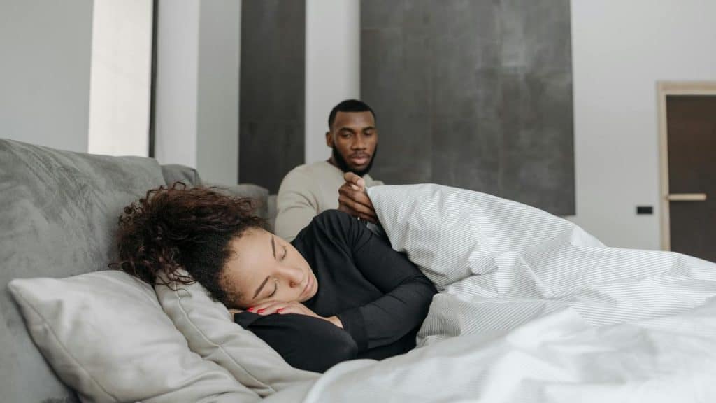 A man gently covering a sleeping person with a blanket.