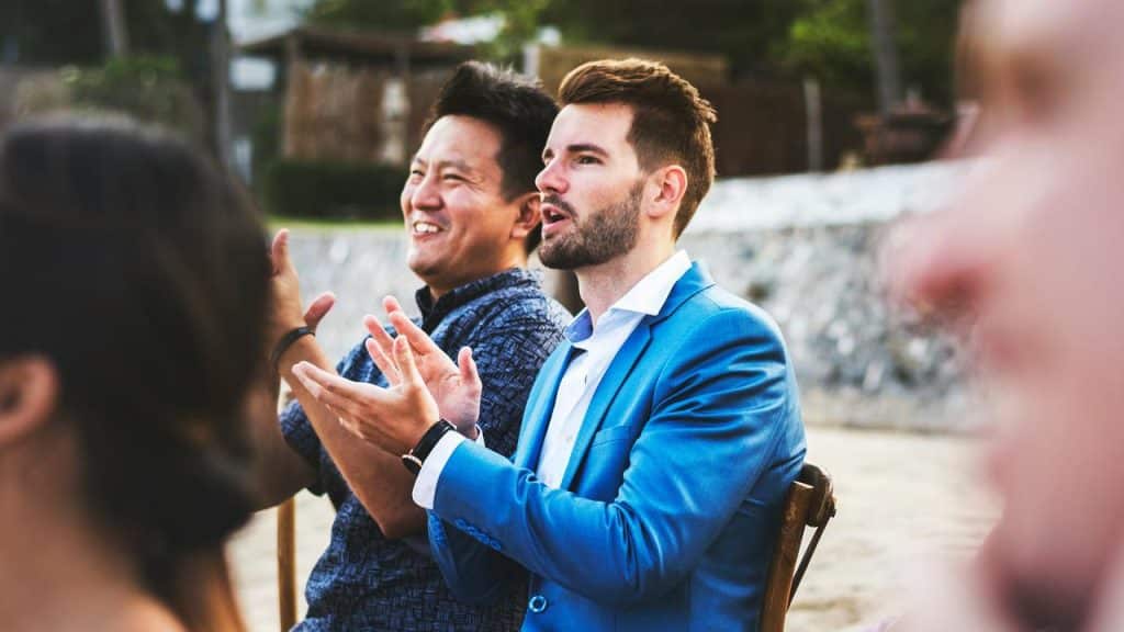 A group of men applauding while seated outdoors at an event.