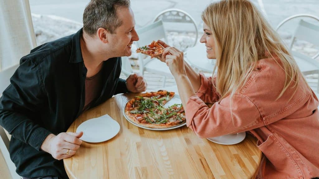 A couple playfully sharing a pizza at an outdoor café.