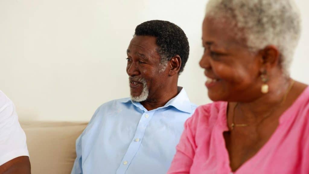 A smiling older couple sitting together and looking toward someone nearby.