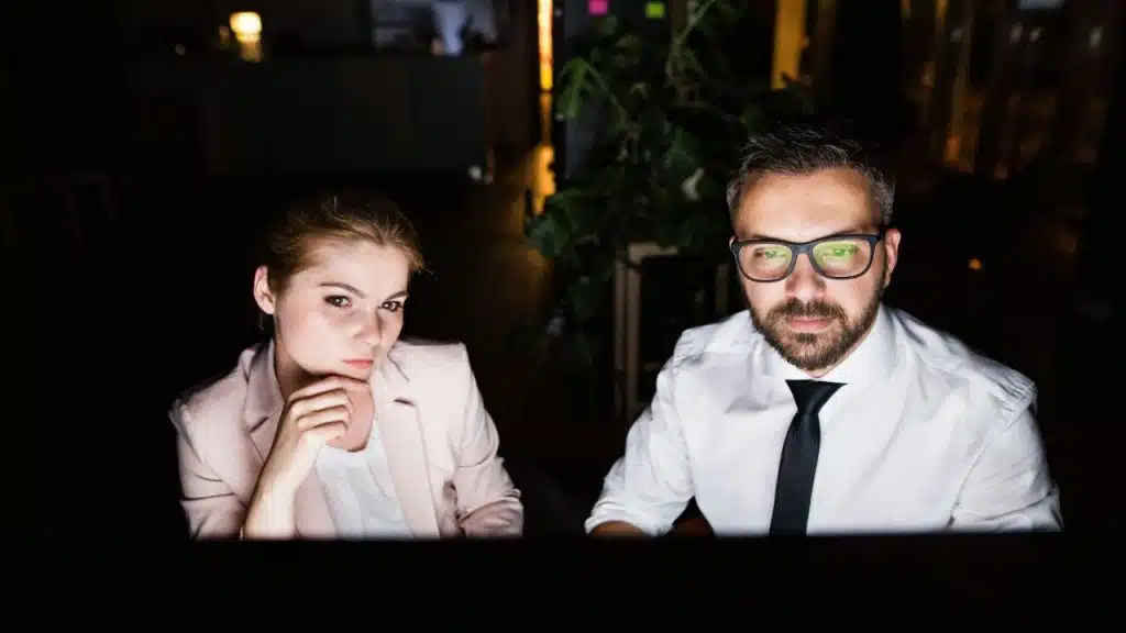 A man and woman sit side-by-side in a dark room, looking at a glowing screen.