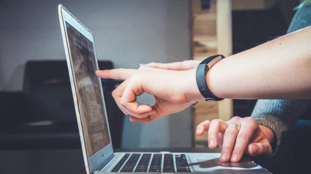A person pointing at a laptop screen while another person types on the keyboard.