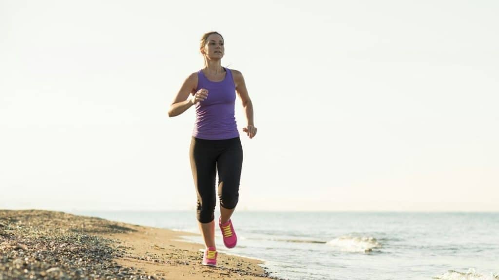 A woman in athletic wear runs along a sandy beach near the ocean water.