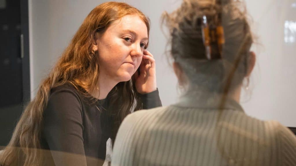 A woman listening intently while speaking with another person indoors.