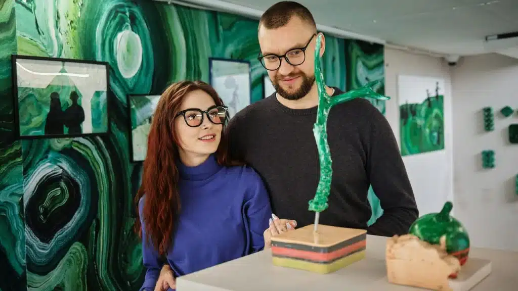 A couple standing in an art gallery, admiring a green abstract sculpture together.