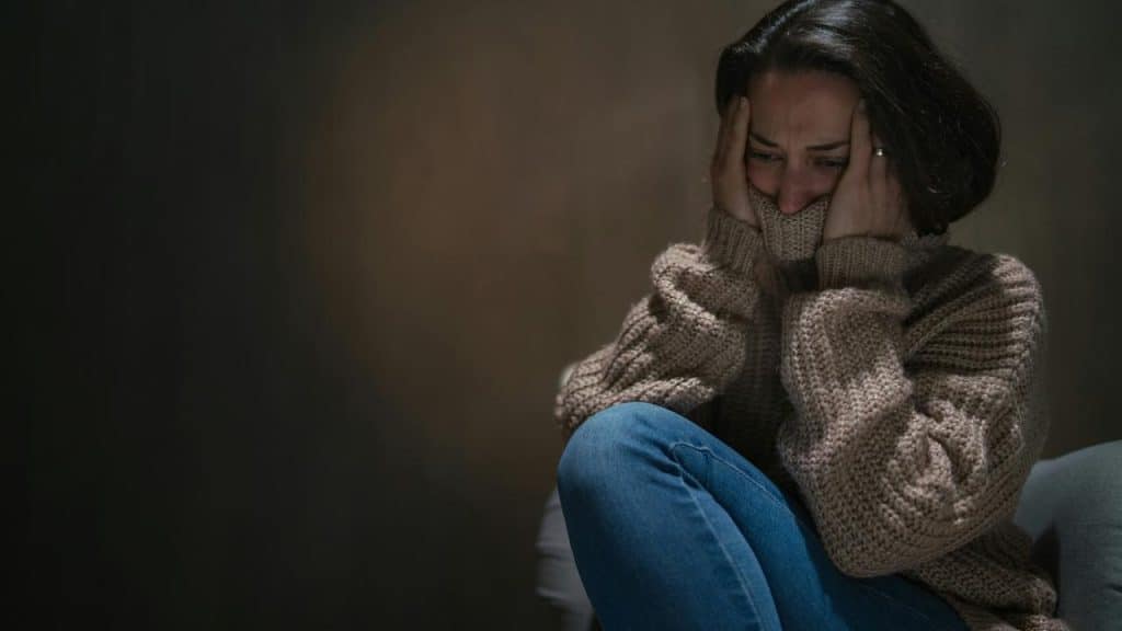 A person sitting with knees drawn up, holding their head in a distressed pose.