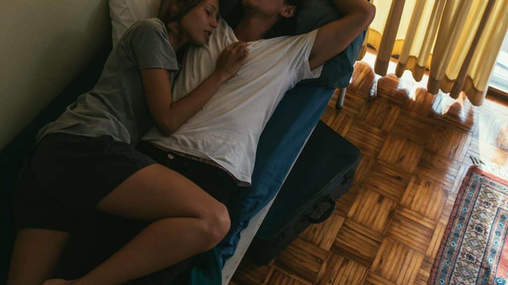 A couple cuddling and resting together on a bed in soft light.