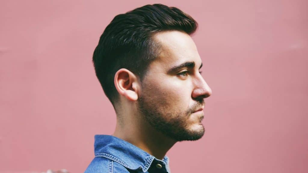 A man in a denim jacket is shown in profile against a solid pink background.