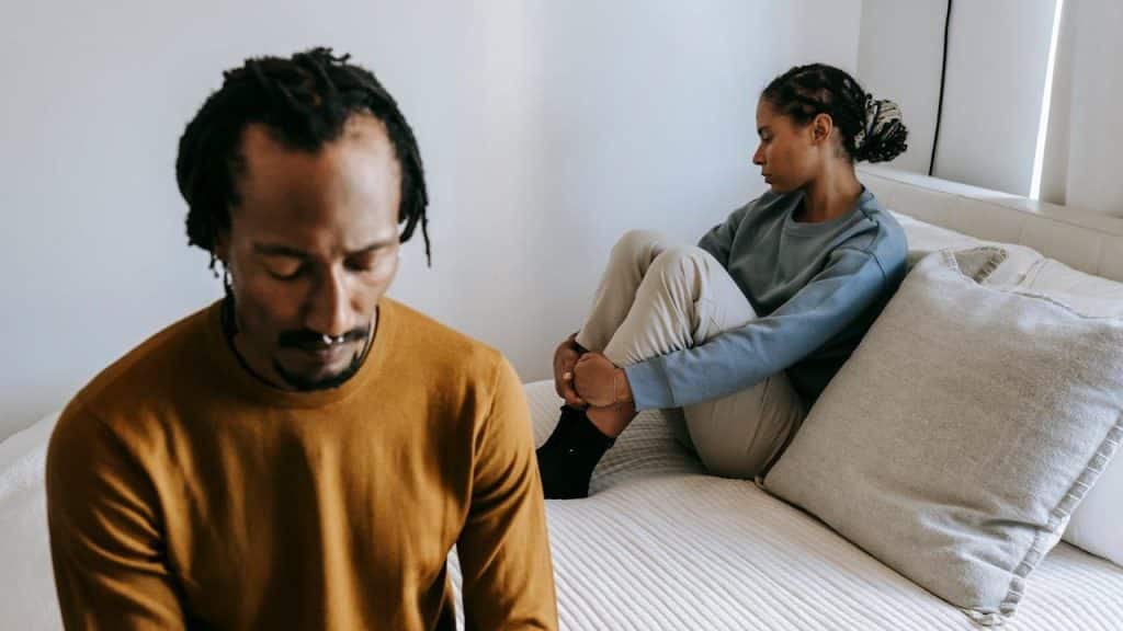 A man and woman sit on a bed with their backs to one another.