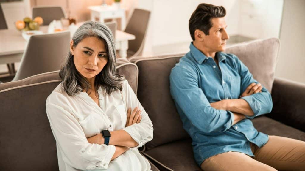 A man and woman sit on a sofa with arms crossed, looking in opposite directions.
