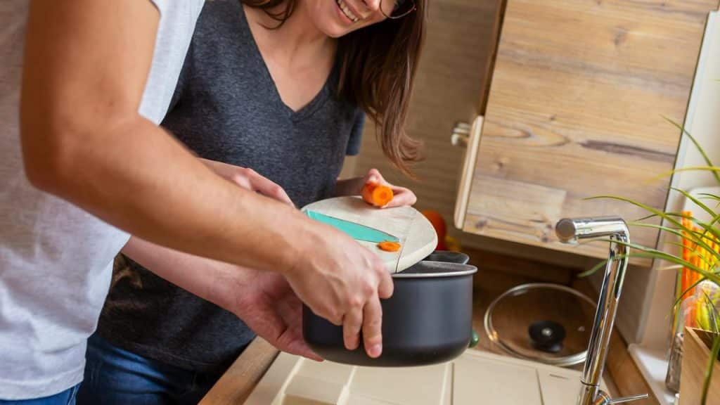 A couple cooking together in a kitchen, adding vegetables to a pot.