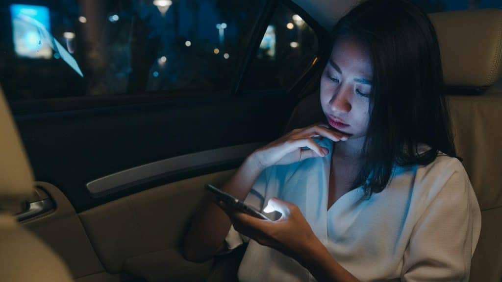 A woman using her phone while sitting in the back seat of a car at night.