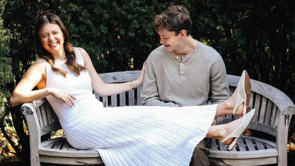 A smiling couple laughing together on a wooden bench outdoors.