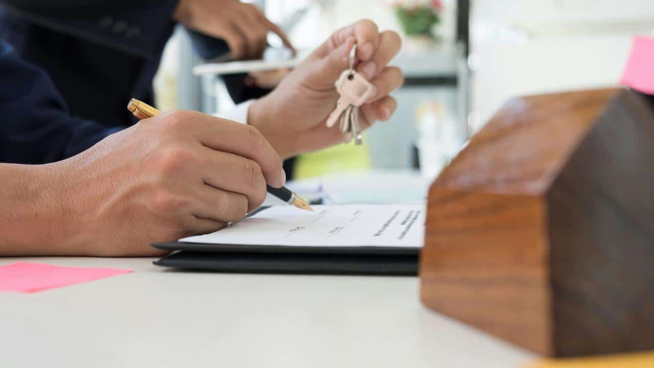 A person signing documents while holding house keys.
