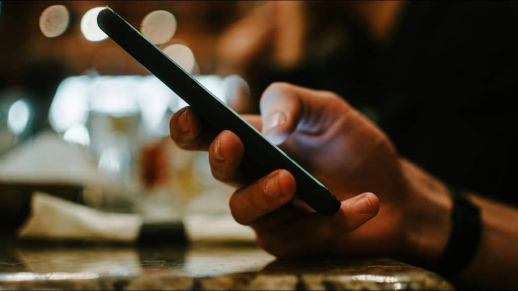 A hand holding a smartphone on a table in a dimly lit setting.