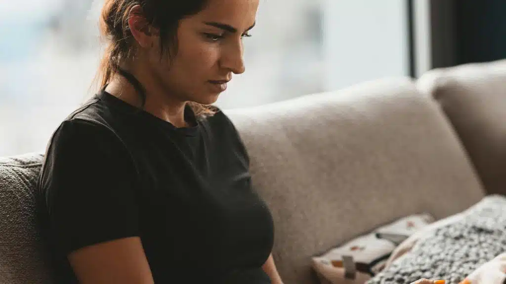 A woman sitting on a couch, looking down with a focused expression.