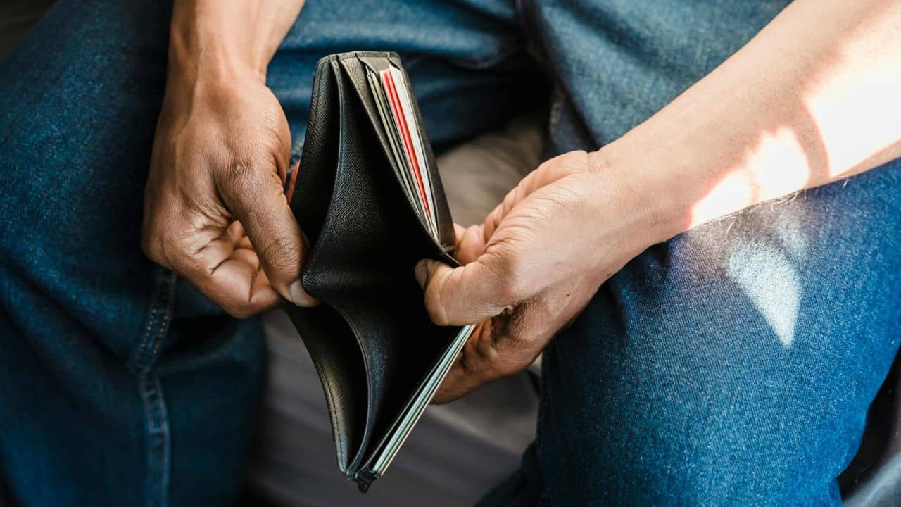 Close-up of a person's hands holding open an empty black leather wallet over blue jeans.