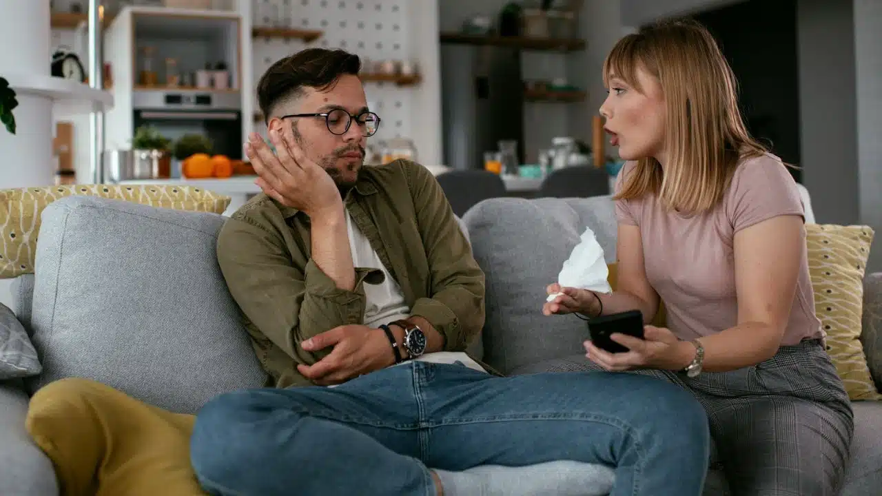 A woman talks to a man who is looking away while sitting on a couch.