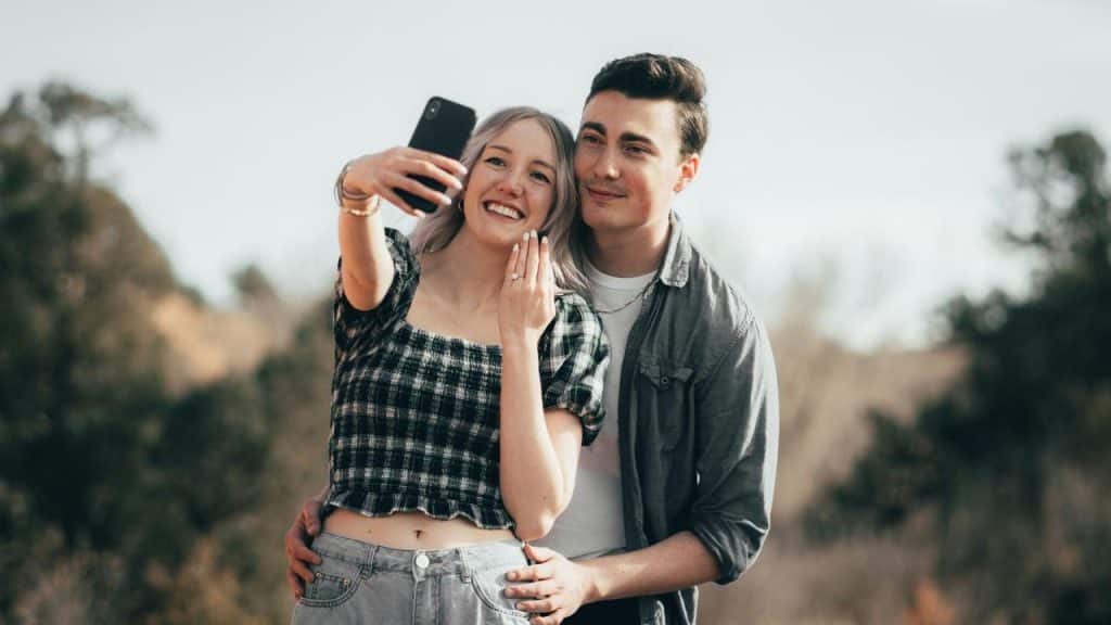 A young couple taking a selfie together outdoors and smiling.