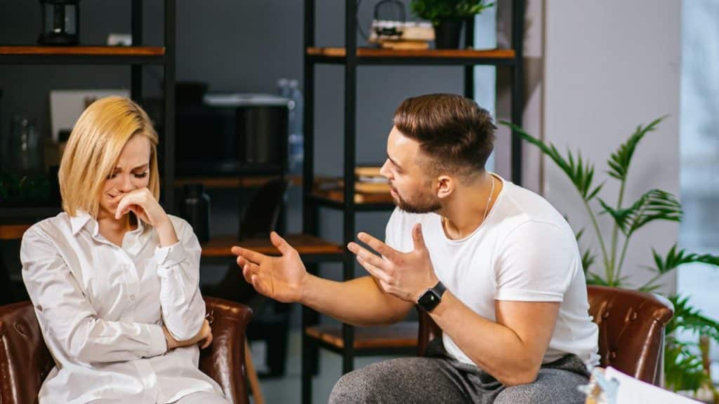 A man gestures while speaking to a woman who is covering her face and crying.