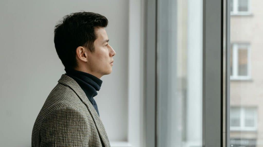 A man in a patterned blazer and turtleneck looks out of a large window.