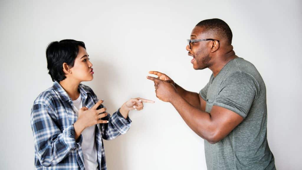 A man and woman stand facing each other while gesturing and pointing during a conversation.