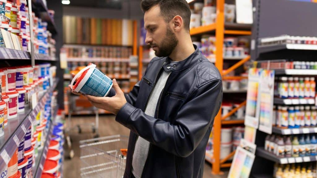 A man in a store aisle reading the label on a container.