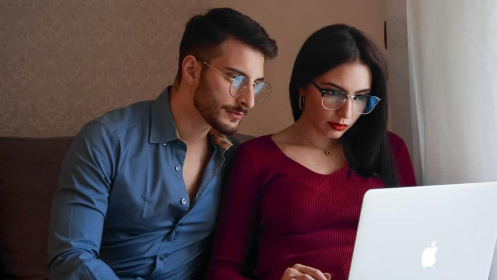 A man and woman wearing glasses look intently at a laptop screen together in a room.