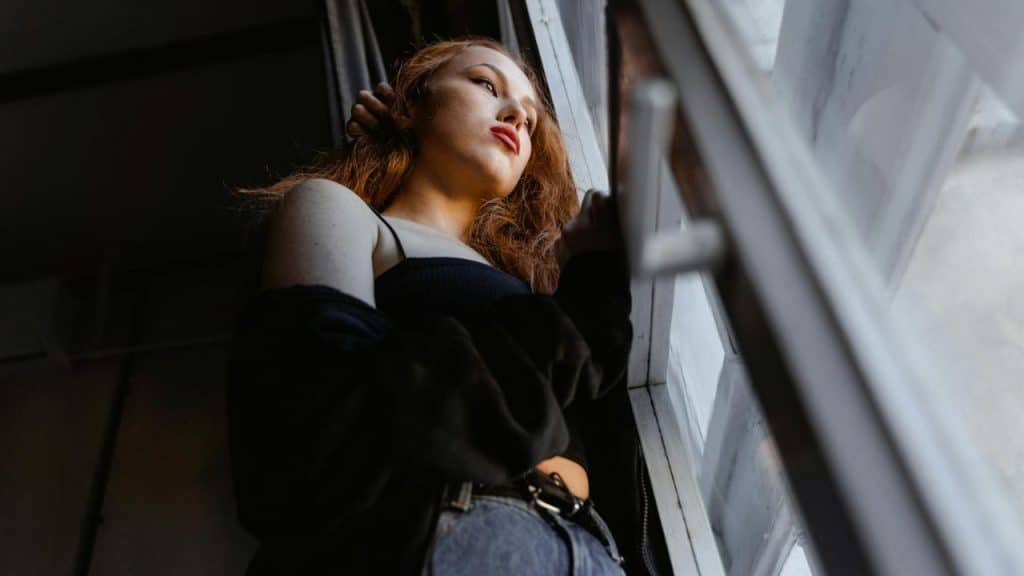 A woman with reddish hair looks out of a window from a low-angle perspective.