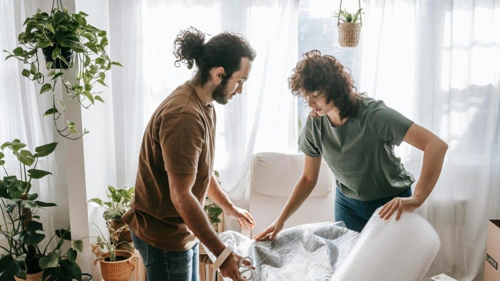 A man and a woman packing items with bubble wrap in a bright room.